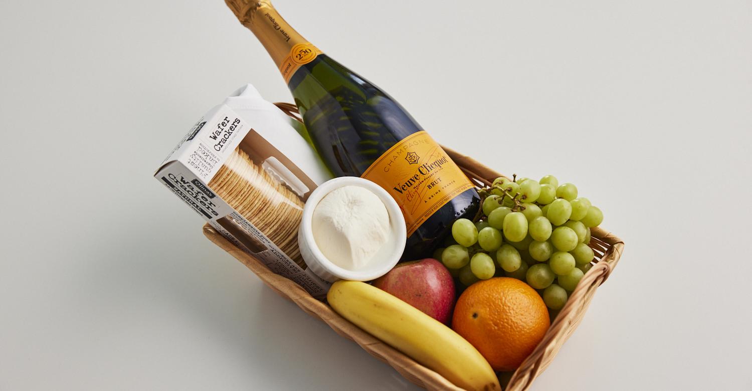 Basket filled with fruits, cheese, crackers, and champagne.