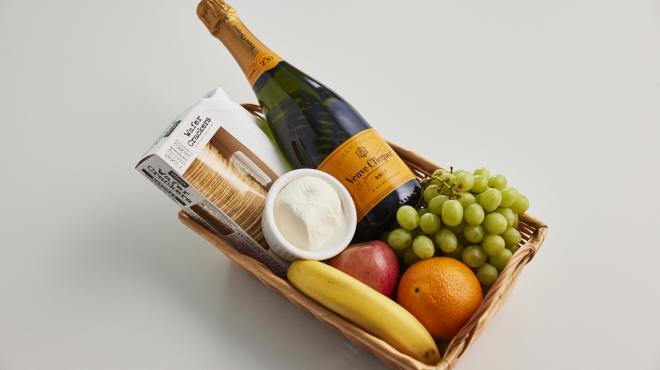 Basket filled with fruits, cheese, crackers, and champagne.