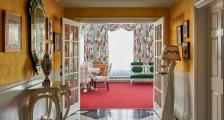 The vibrant interior of the Carleton Varney Suite at Grand Hotel, showing the view from a yellow parlor through to a sitting room with bold red carpet.