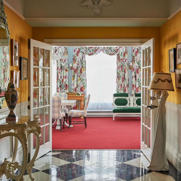 The vibrant interior of the Carleton Varney Suite at Grand Hotel, showing the view from a yellow parlor through to a sitting room with bold red carpet.