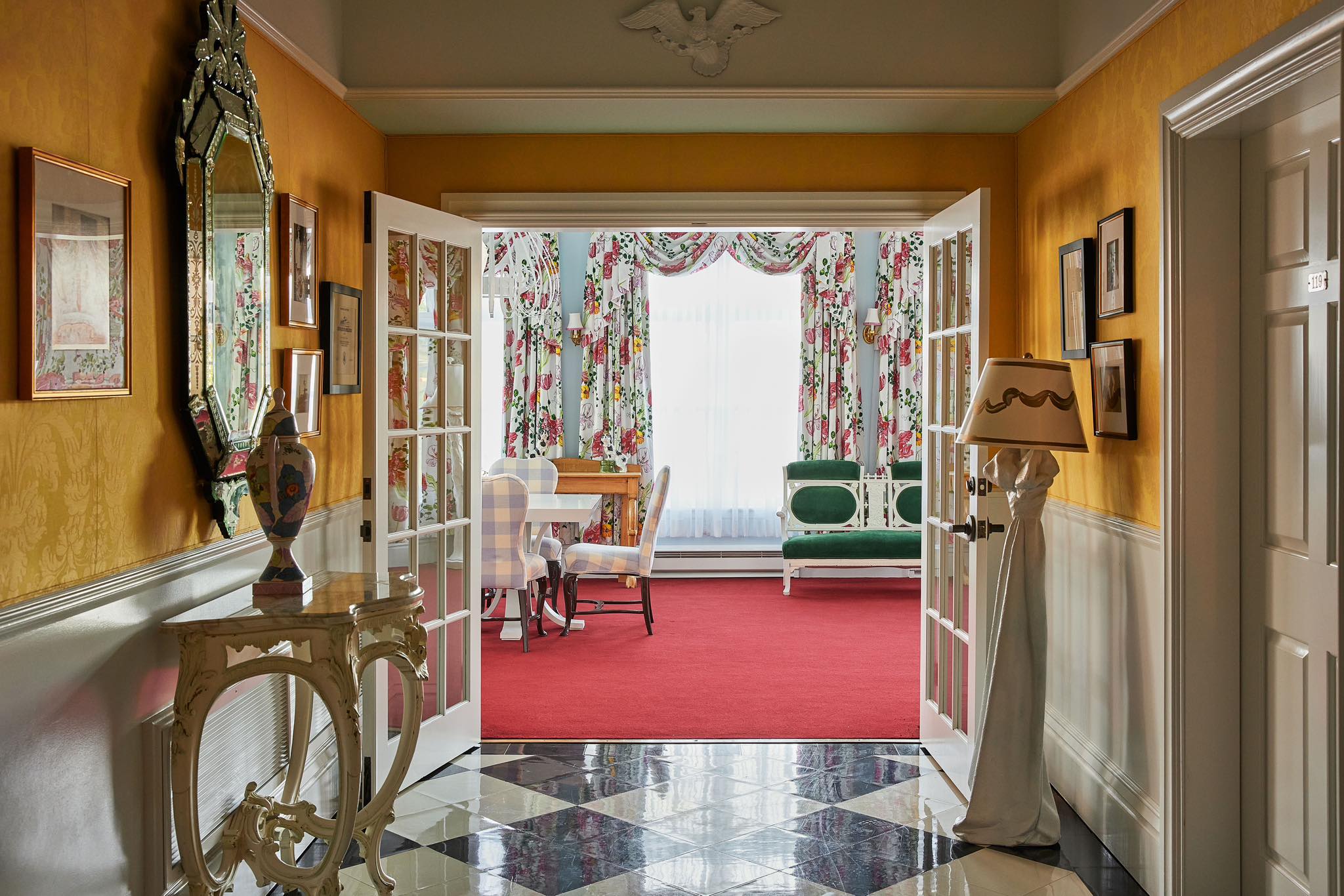 The vibrant interior of the Carleton Varney Suite at Grand Hotel, showing the view from a yellow parlor through to a sitting room with bold red carpet.