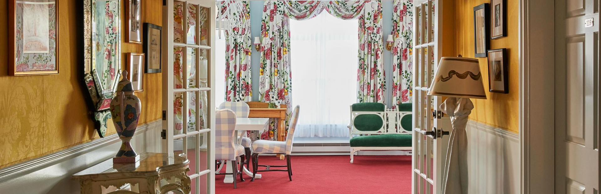 The vibrant interior of the Carleton Varney Suite at Grand Hotel, showing the view from a yellow parlor through to a sitting room with bold red carpet.