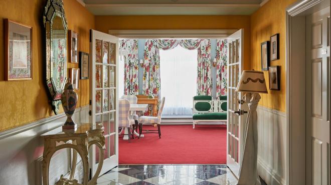 The vibrant interior of the Carleton Varney Suite at Grand Hotel, showing the view from a yellow parlor through to a sitting room with bold red carpet.
