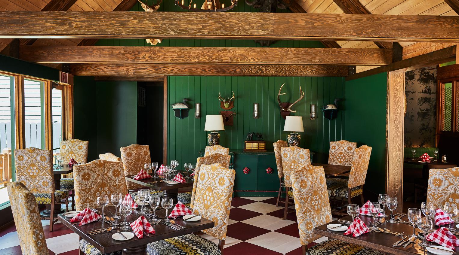 The unique, Bavarian-themed interior of The Woods restaurant, a Grand Hotel dining destination on Mackinac Island, featuring green walls, antlers, and a bold checkered floor.