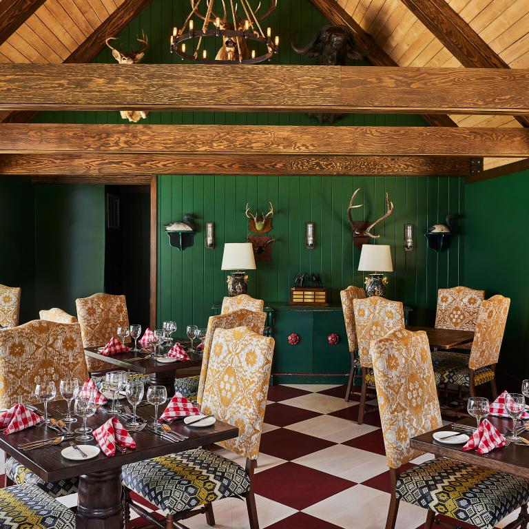The unique, Bavarian-themed interior of The Woods restaurant, a Grand Hotel dining destination on Mackinac Island, featuring green walls, antlers, and a bold checkered floor.