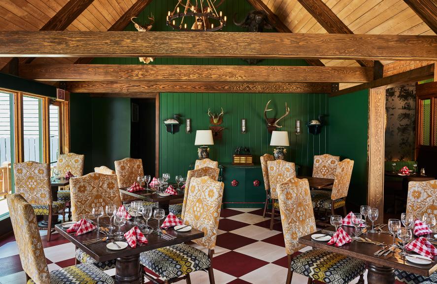 The unique, Bavarian-themed interior of The Woods restaurant, a Grand Hotel dining destination on Mackinac Island, featuring green walls, antlers, and a bold checkered floor.