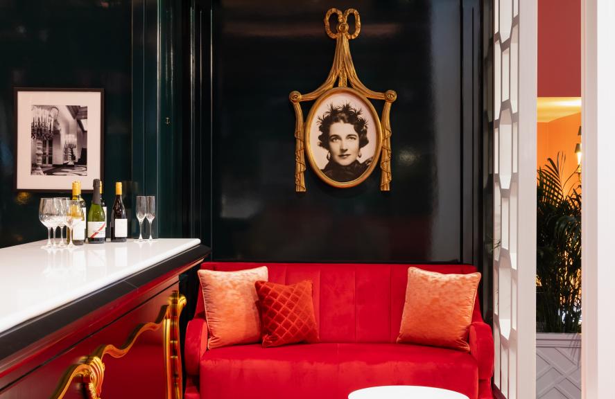 Luxurious lounge with red velvet seating, patterned carpet, cream armchairs, and black lacquered shelving in an elegant upscale interior.