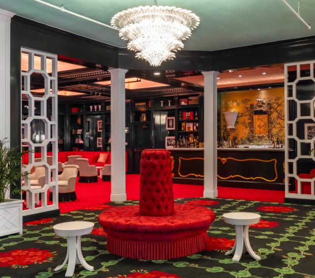 Luxurious lounge with red velvet seating, patterned carpet, cream armchairs, and black lacquered shelving in an elegant upscale interior.