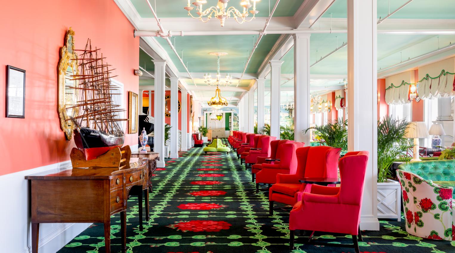 The vibrant and eclectic lobby of Grand Hotel, showcasing the iconic interior design by Carleton Varney, with its scenic mural wallpaper and bold pink and red furniture.