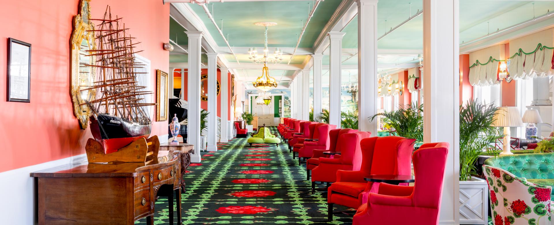 The vibrant and eclectic lobby of Grand Hotel, showcasing the iconic interior design by Carleton Varney, with its scenic mural wallpaper and bold pink and red furniture.