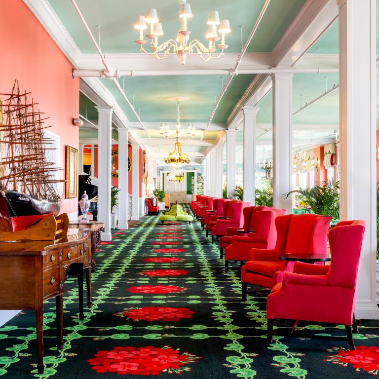The vibrant and eclectic lobby of Grand Hotel, showcasing the iconic interior design by Carleton Varney, with its scenic mural wallpaper and bold pink and red furniture.