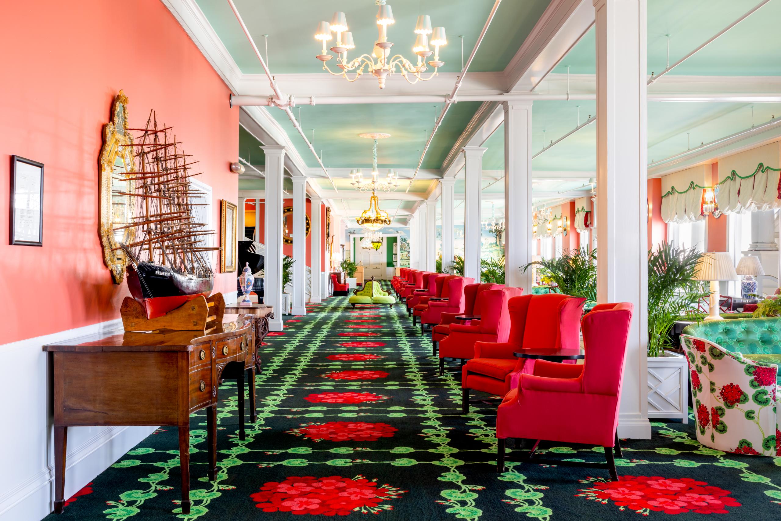 The vibrant and eclectic lobby of Grand Hotel, showcasing the iconic interior design by Carleton Varney, with its scenic mural wallpaper and bold pink and red furniture.