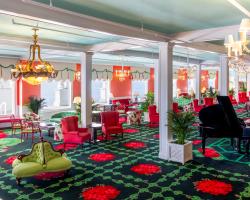 The vibrant and eclectic lobby of Grand Hotel, showcasing the iconic interior design by Carleton Varney, with its scenic mural wallpaper and bold pink and red furniture.