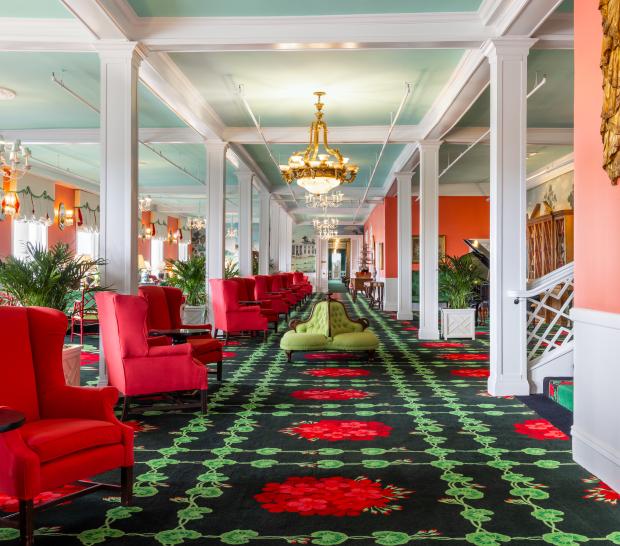 The vibrant and eclectic lobby of Grand Hotel, showcasing the iconic interior design by Carleton Varney, with its scenic mural wallpaper and bold pink and red furniture.