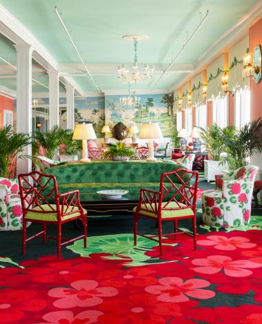The vibrant and eclectic lobby of Grand Hotel, showcasing the iconic interior design by Carleton Varney, with its scenic mural wallpaper and bold pink and red furniture.