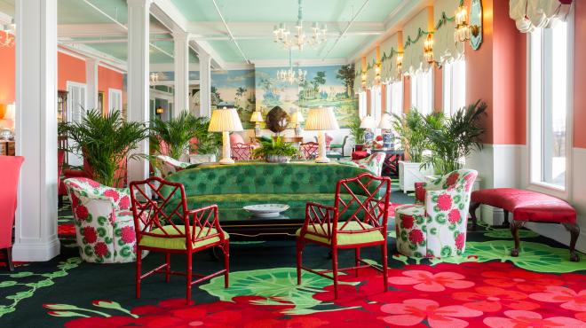 The vibrant and eclectic lobby of Grand Hotel, showcasing the iconic interior design by Carleton Varney, with its scenic mural wallpaper and bold pink and red furniture.