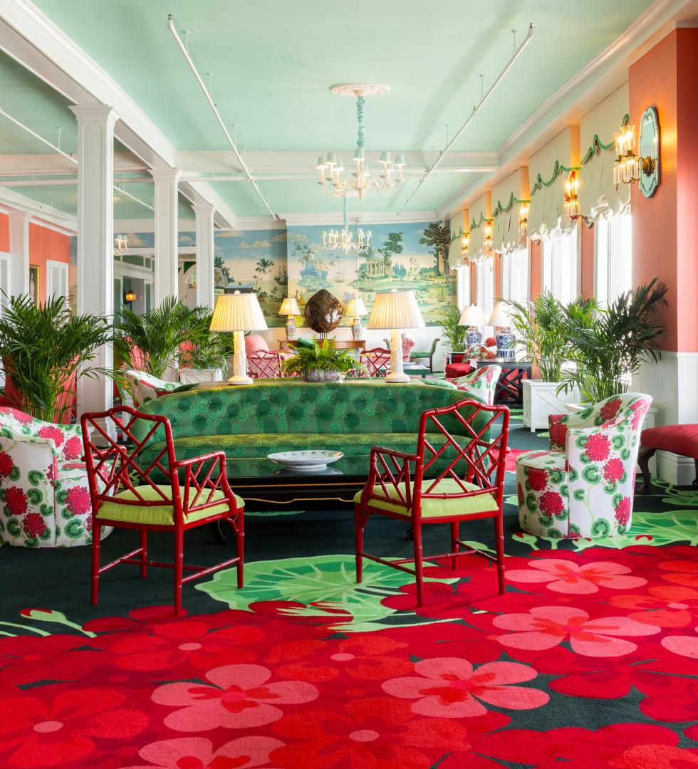 The vibrant and eclectic lobby of Grand Hotel, showcasing the iconic interior design by Carleton Varney, with its scenic mural wallpaper and bold pink and red furniture.