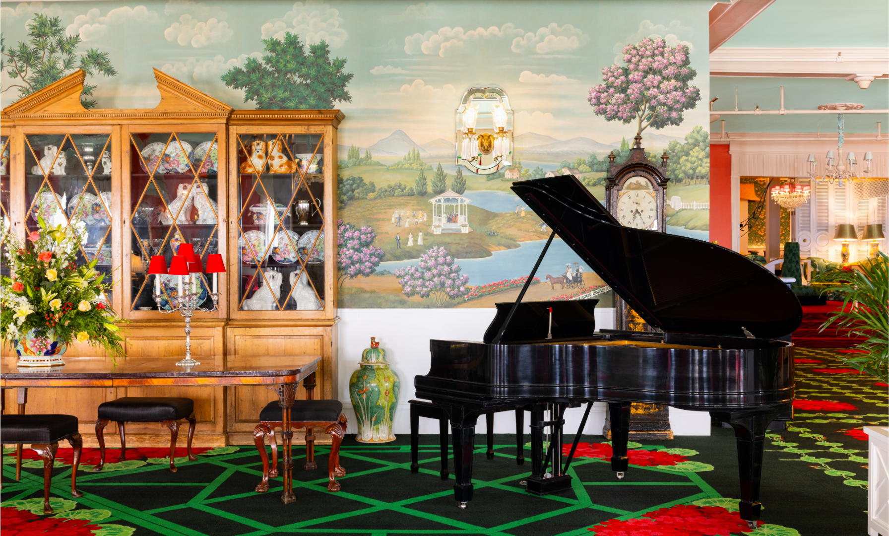 The vibrant and eclectic lobby of Grand Hotel, showcasing the iconic interior design by Carleton Varney, with its scenic mural wallpaper and bold pink and red furniture.
