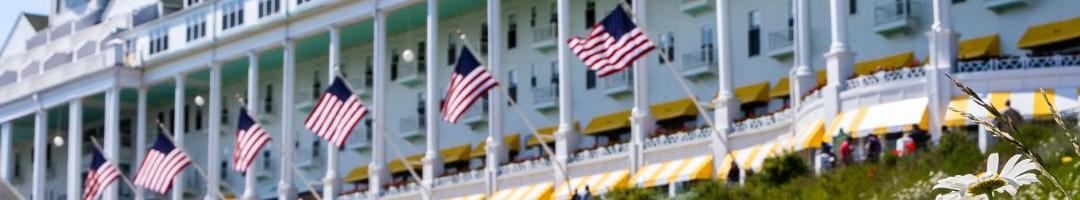 A beautiful low-angle view of the historic Grand Hotel on Mackinac Island, looking up through a field of white daisies on a sunny summer day.