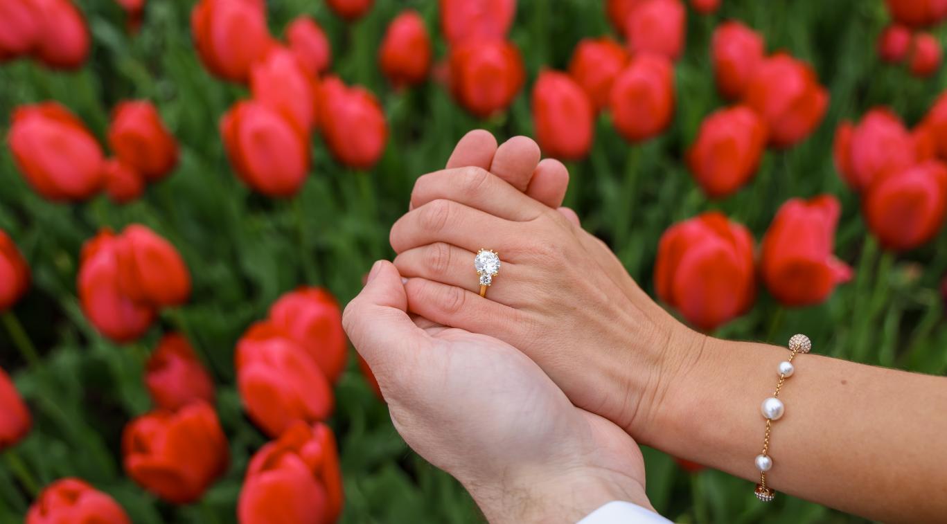 A proposal image in front of tulips. Highlighting the engagement ring.