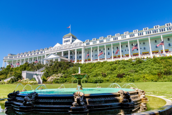 Front view of a large white hotel with a green roof, flagpoles with American flags along the facade, and a decorative fountain in the foreground.